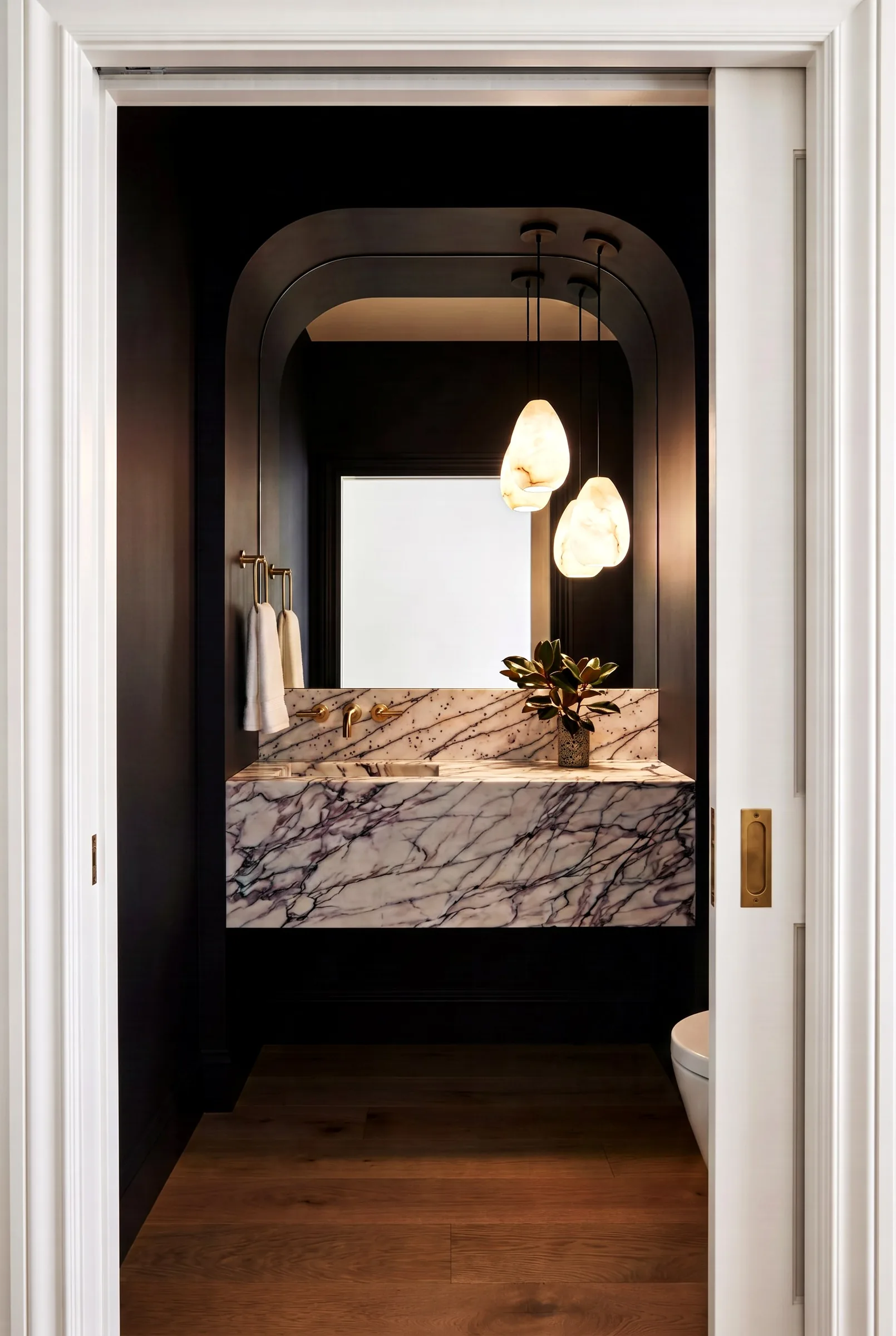 Photoreal render of a powder room with a floating violet-veined marble sink, alabaster pendants and an arched mirror